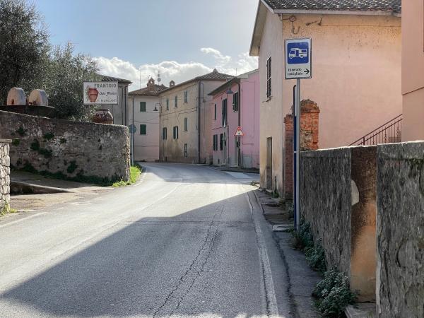 Entrée de San Feliciano par une route pavée entre des maisons pastel. Un panneau indique un « itinéraire recommandé » pour les camping-cars.